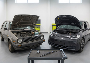 Petrol and electric hatchbacks with raised bonnets beside a tyre gauge and replacement wiper blade in an inspection bay.
